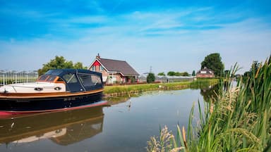 A narrow canal with a boat docked on the left, surrounded by greenery and houses.