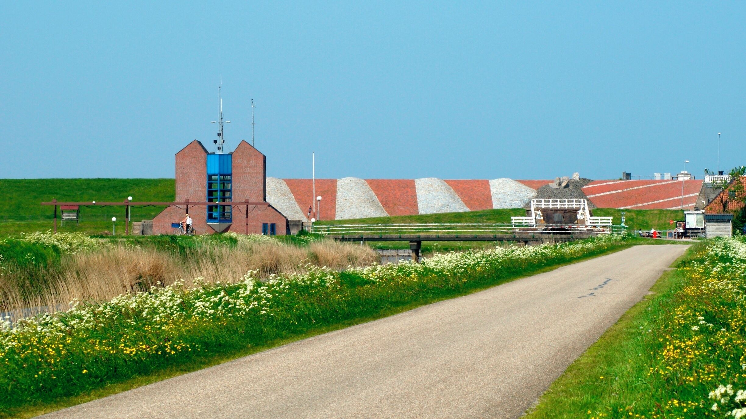 A rural road with a brick building, a blue tower, and a large pile of gravel.
