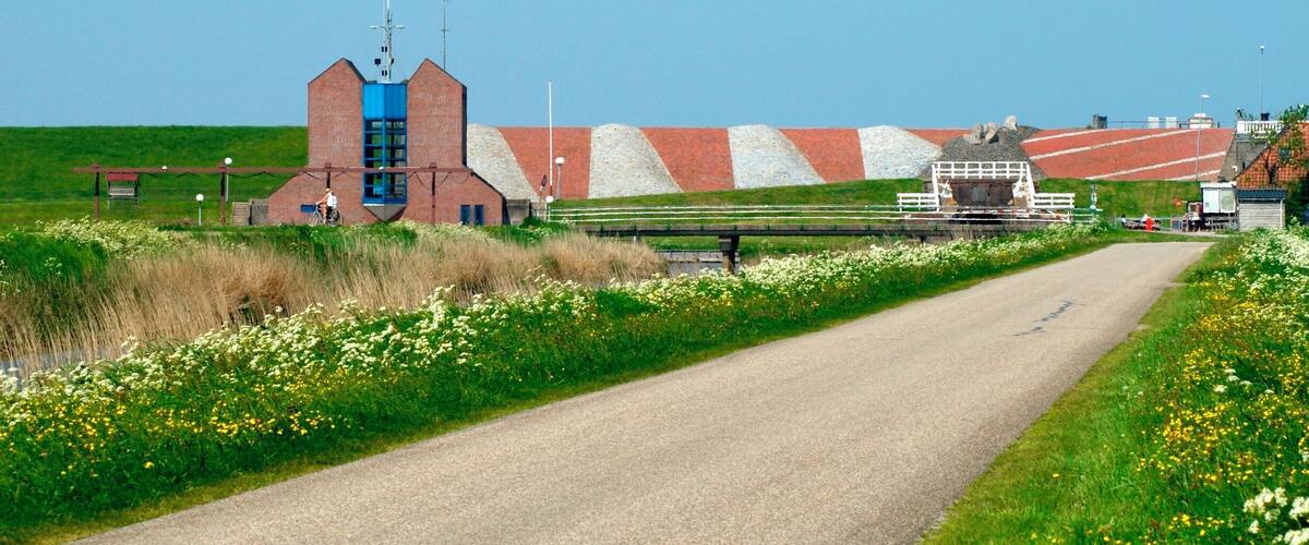 A rural road with a brick building, a blue tower, and a large pile of gravel.