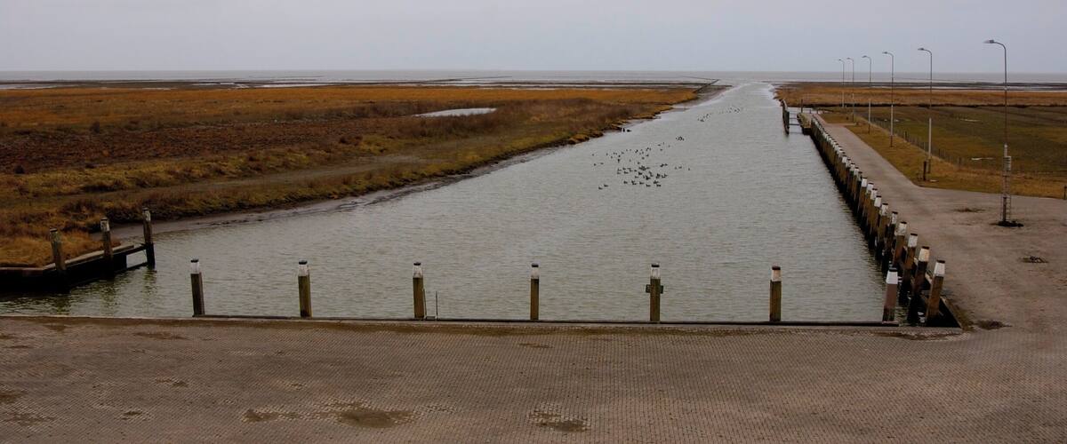 A canal with a lock system, surrounded by marshland and a cloudy sky.