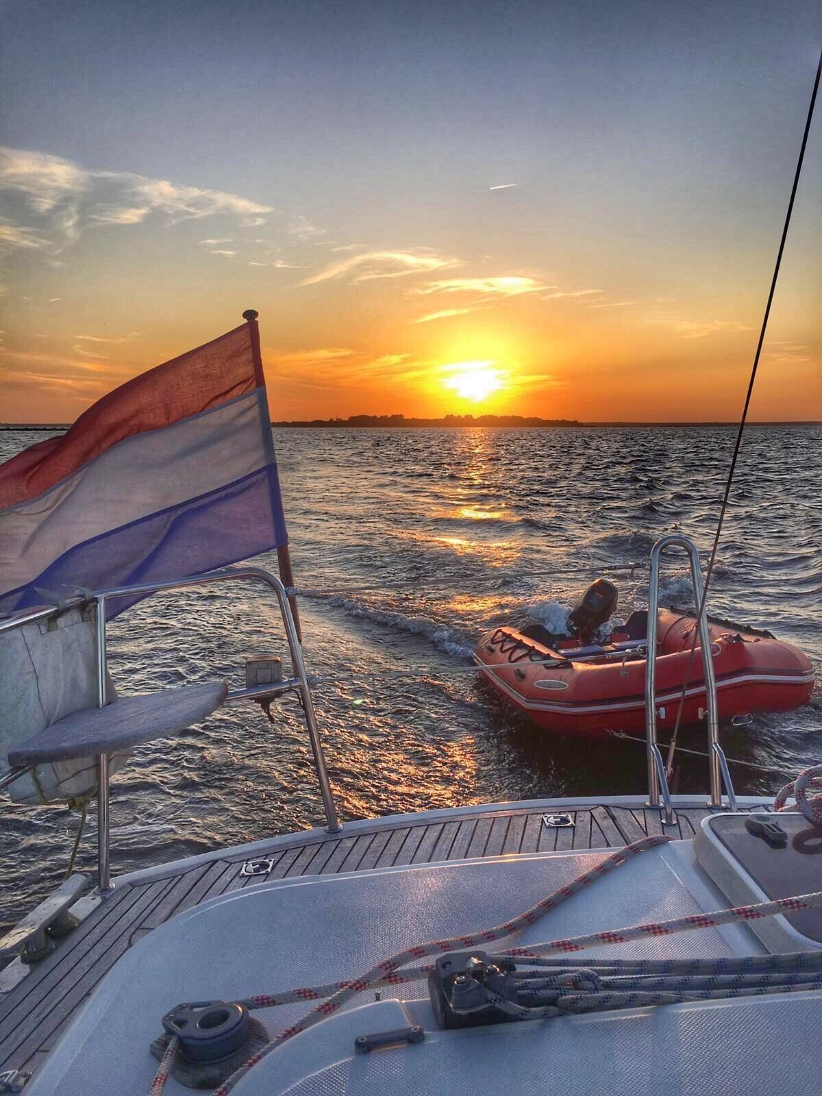 A sunset over the ocean with a boat and a red inflatable dinghy.