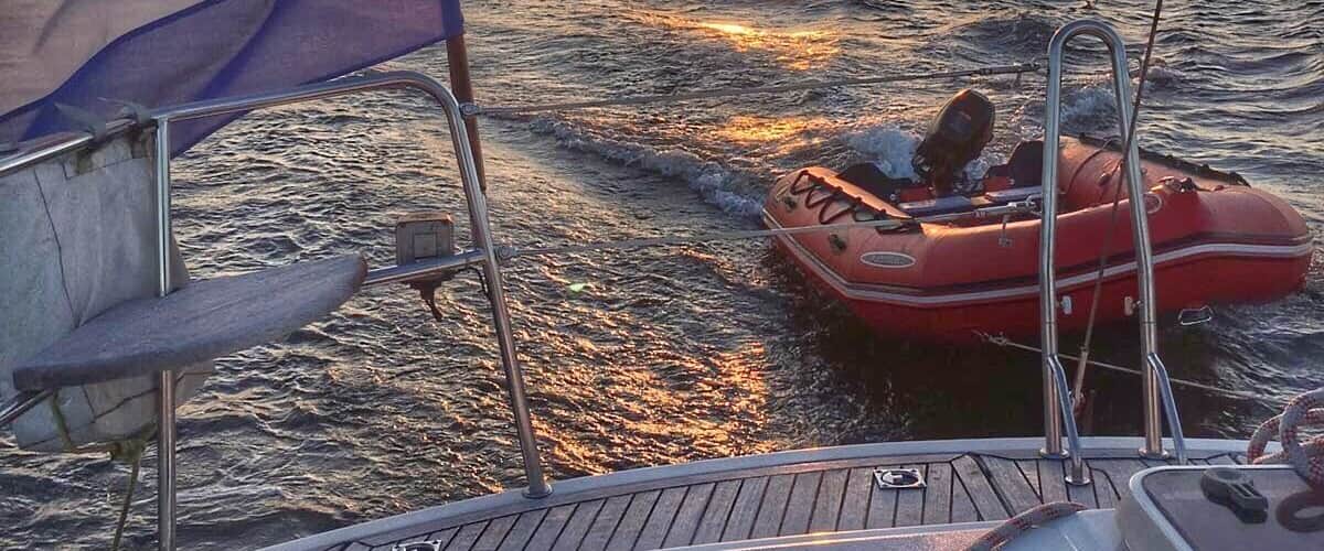 A sunset over the ocean with a boat and a red inflatable dinghy.