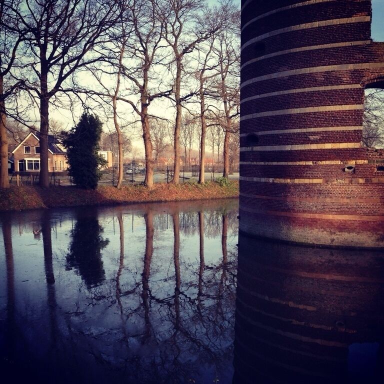 A river reflecting trees and a brick structure.