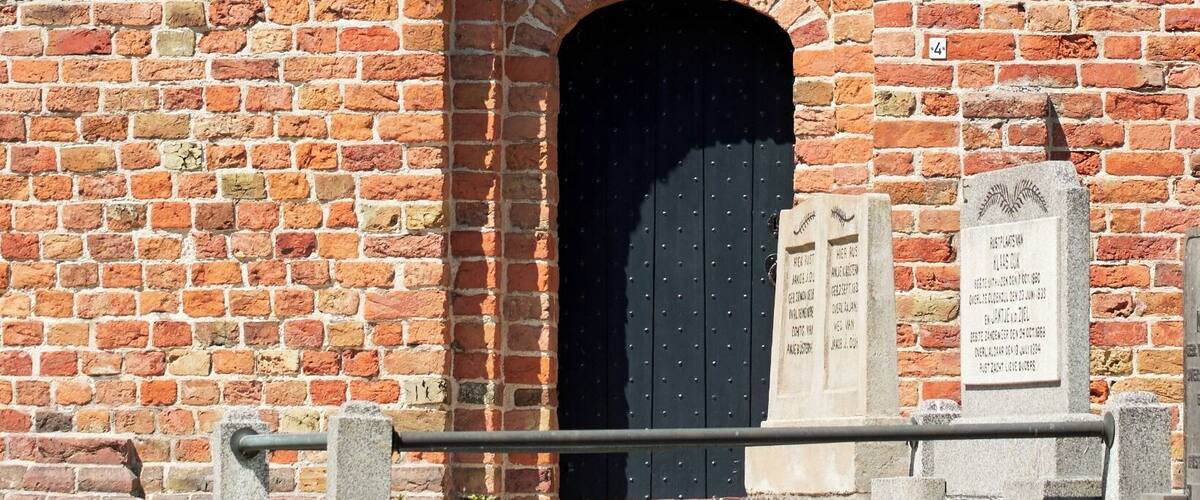 En murstensbygning med en sort dør og et buet vindue. To stenplader ligger foran.