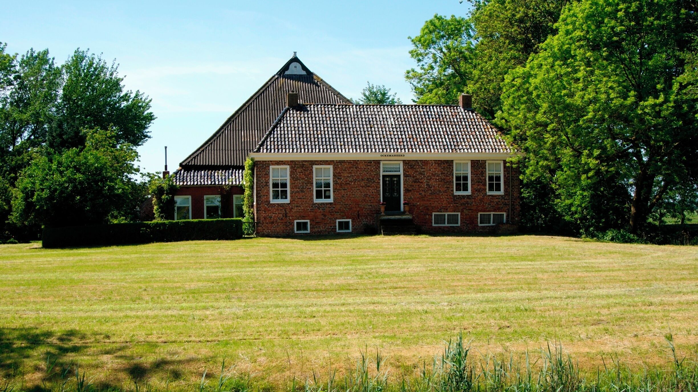 A large brick house with a tiled roof and a grassy field in front.