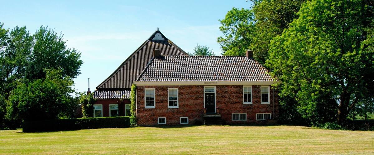 A large brick house with a tiled roof and a grassy field in front.