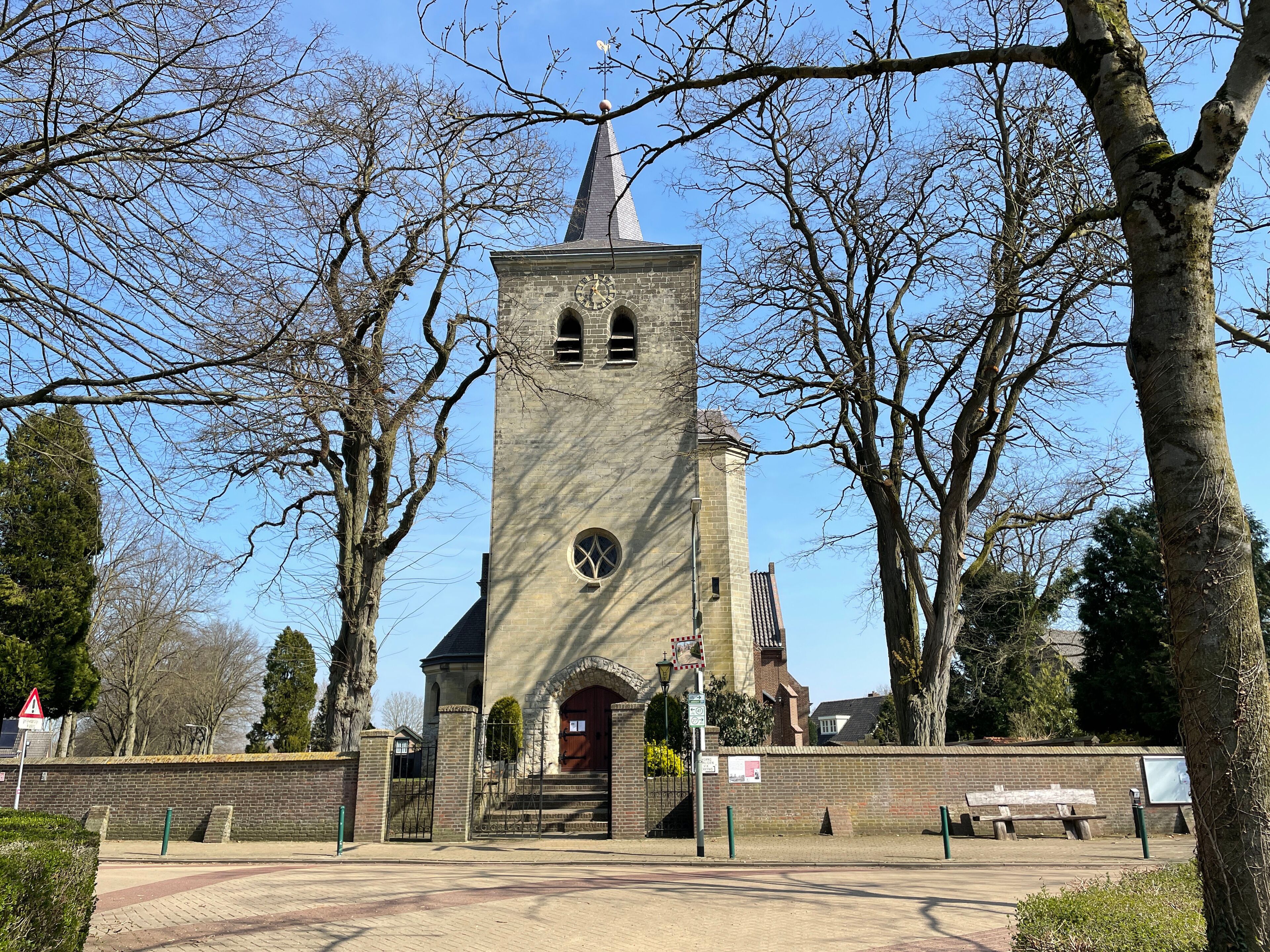 A church with a tall tower, surrounded by trees and a brick wall.