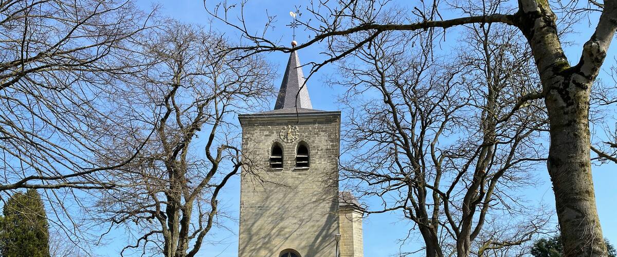 A church with a tall tower, surrounded by trees and a brick wall.