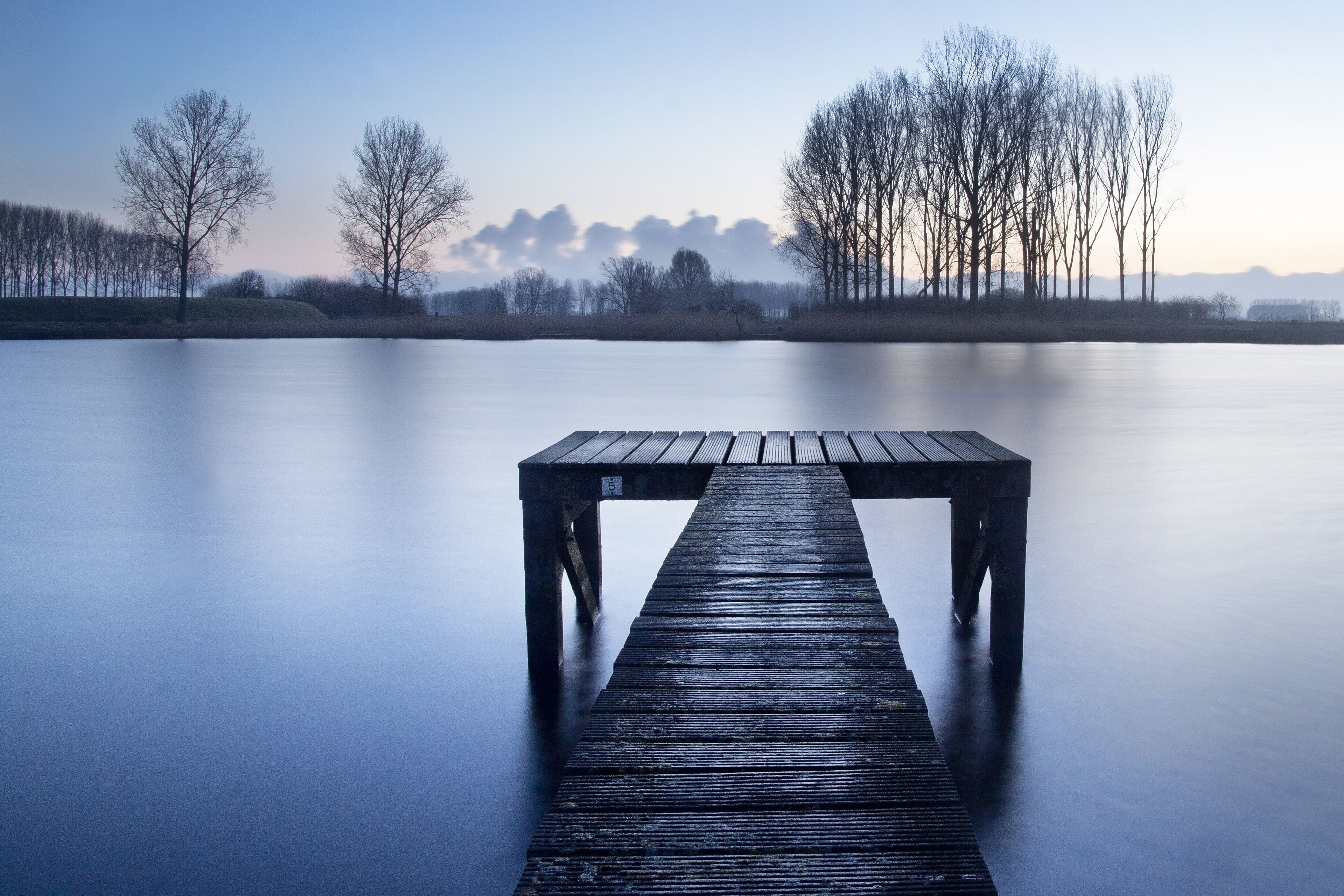 A wooden pier extending into a calm lake with bare trees in the background.