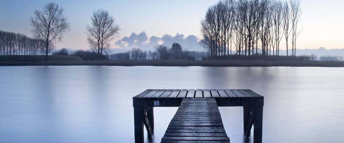 A wooden pier extending into a calm lake with bare trees in the background.