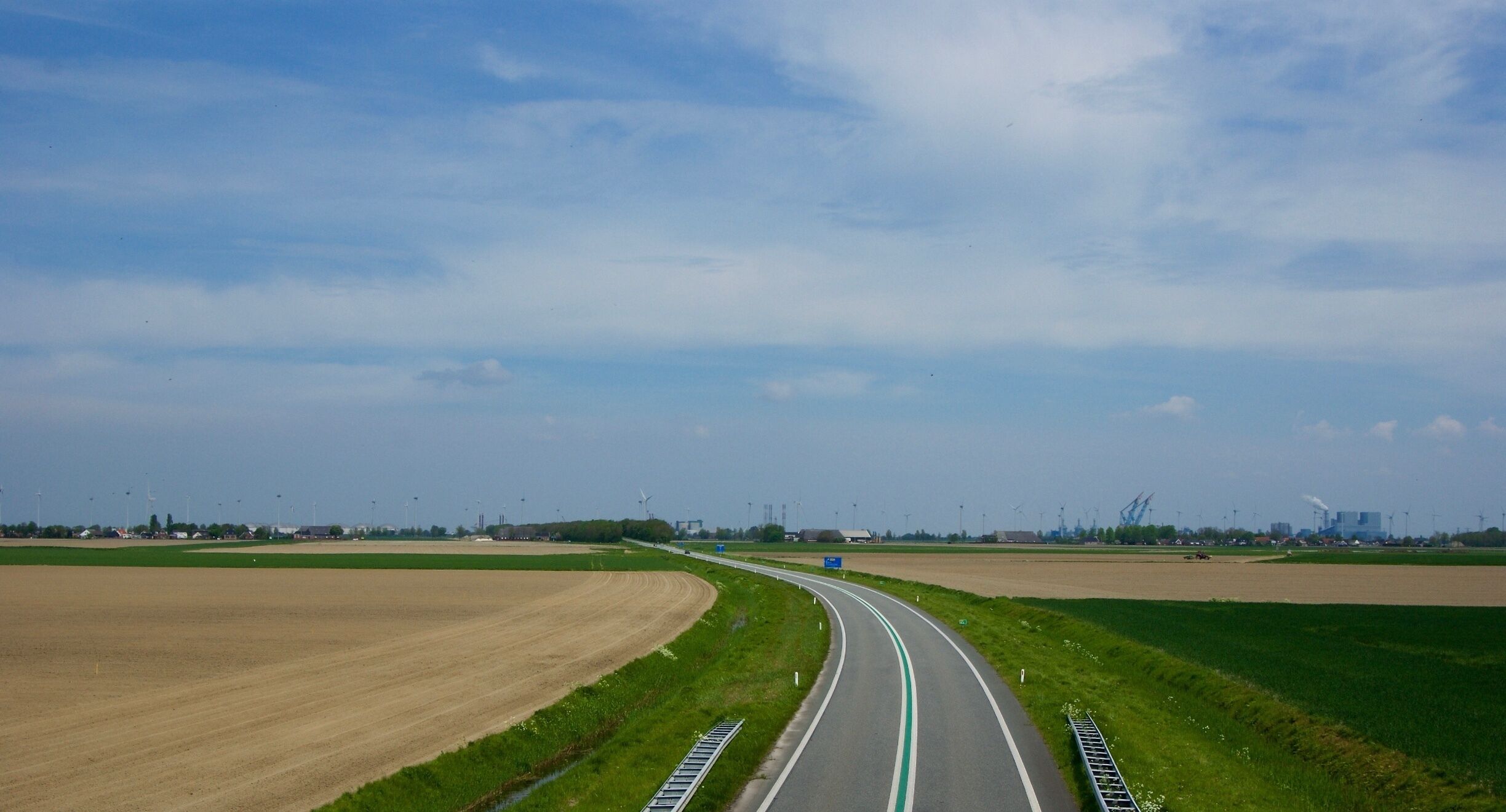 A highway curving through agricultural fields with wind turbines in the distance.