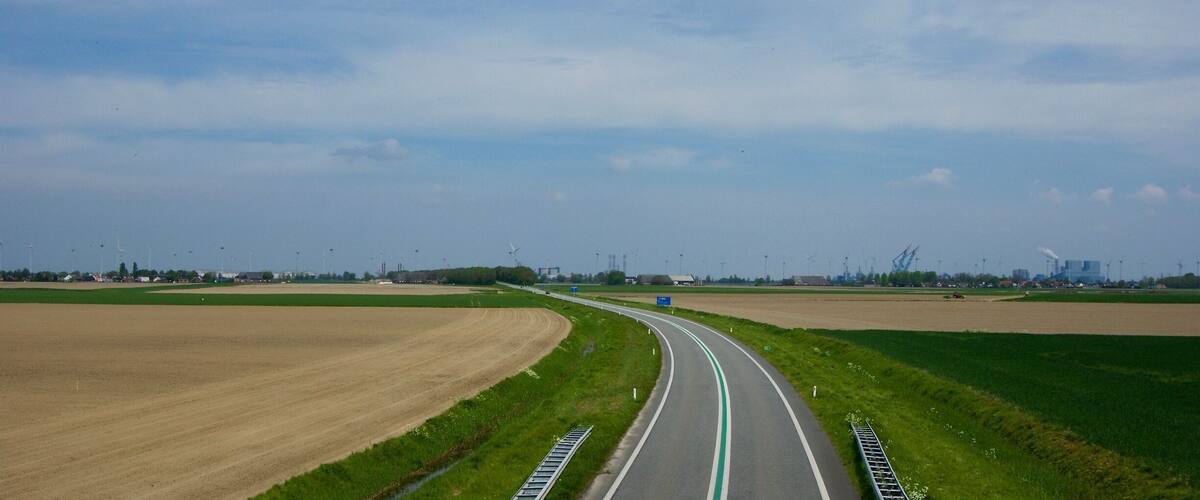 A highway curving through agricultural fields with wind turbines in the distance.