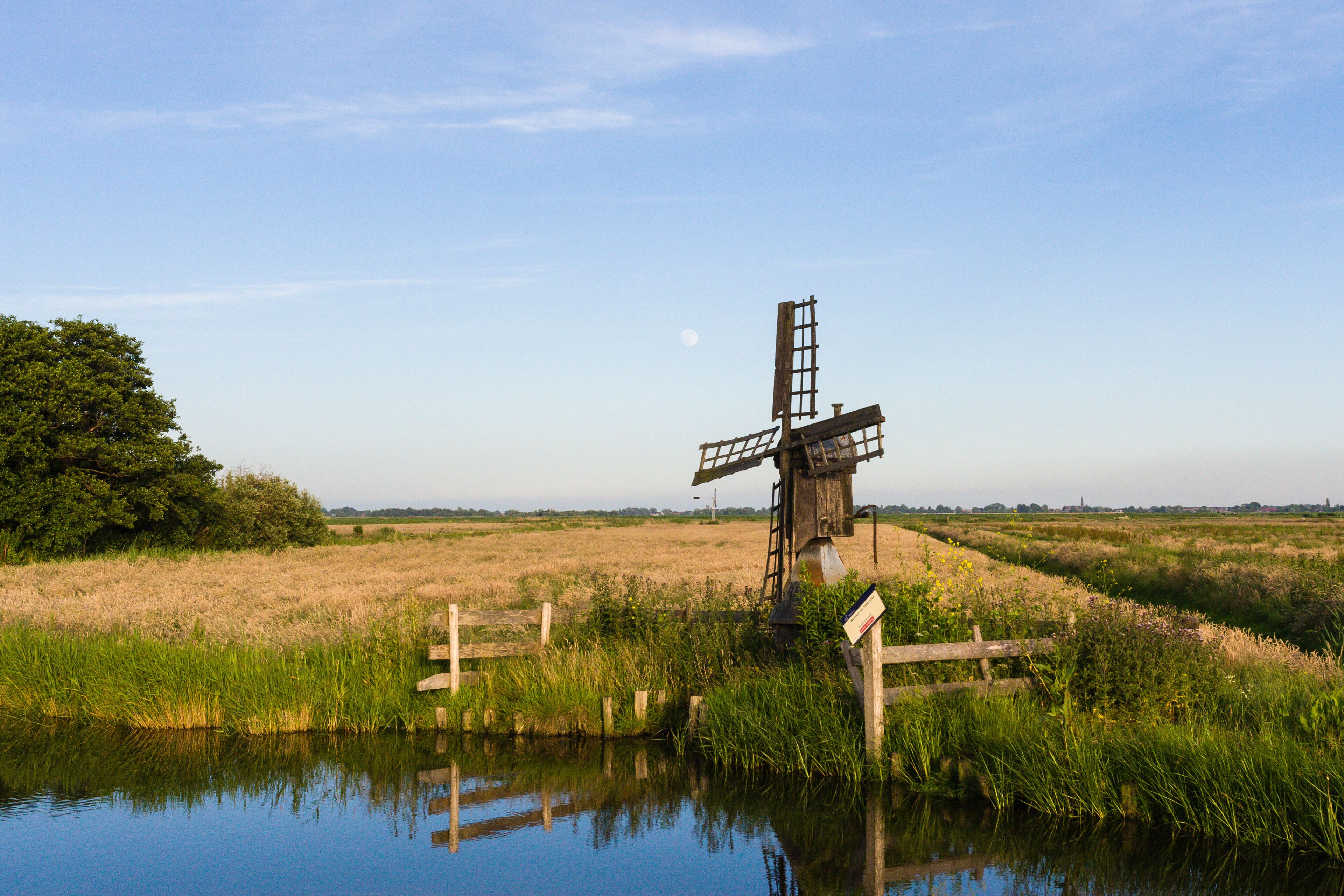 A windmill in a field with a body of water in the foreground.