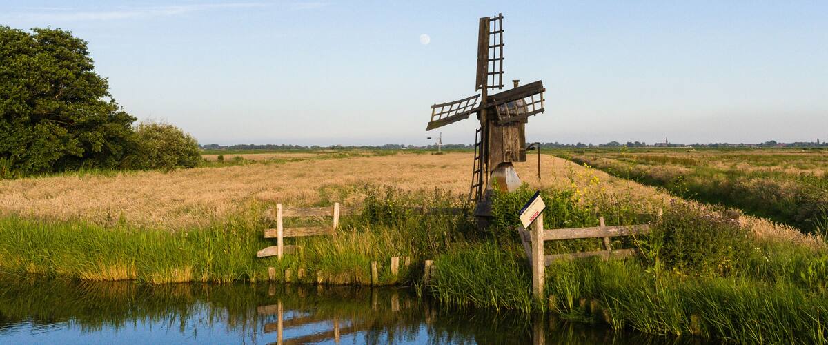 A windmill in a field with a body of water in the foreground.