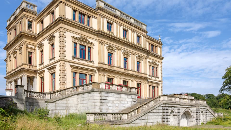 A historic building with classical architecture, a stone staircase, and a small bridge.
