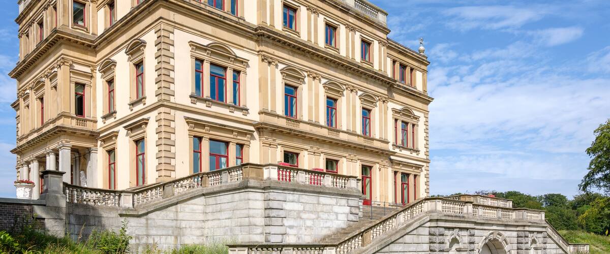 A historic building with classical architecture, a stone staircase, and a small bridge.