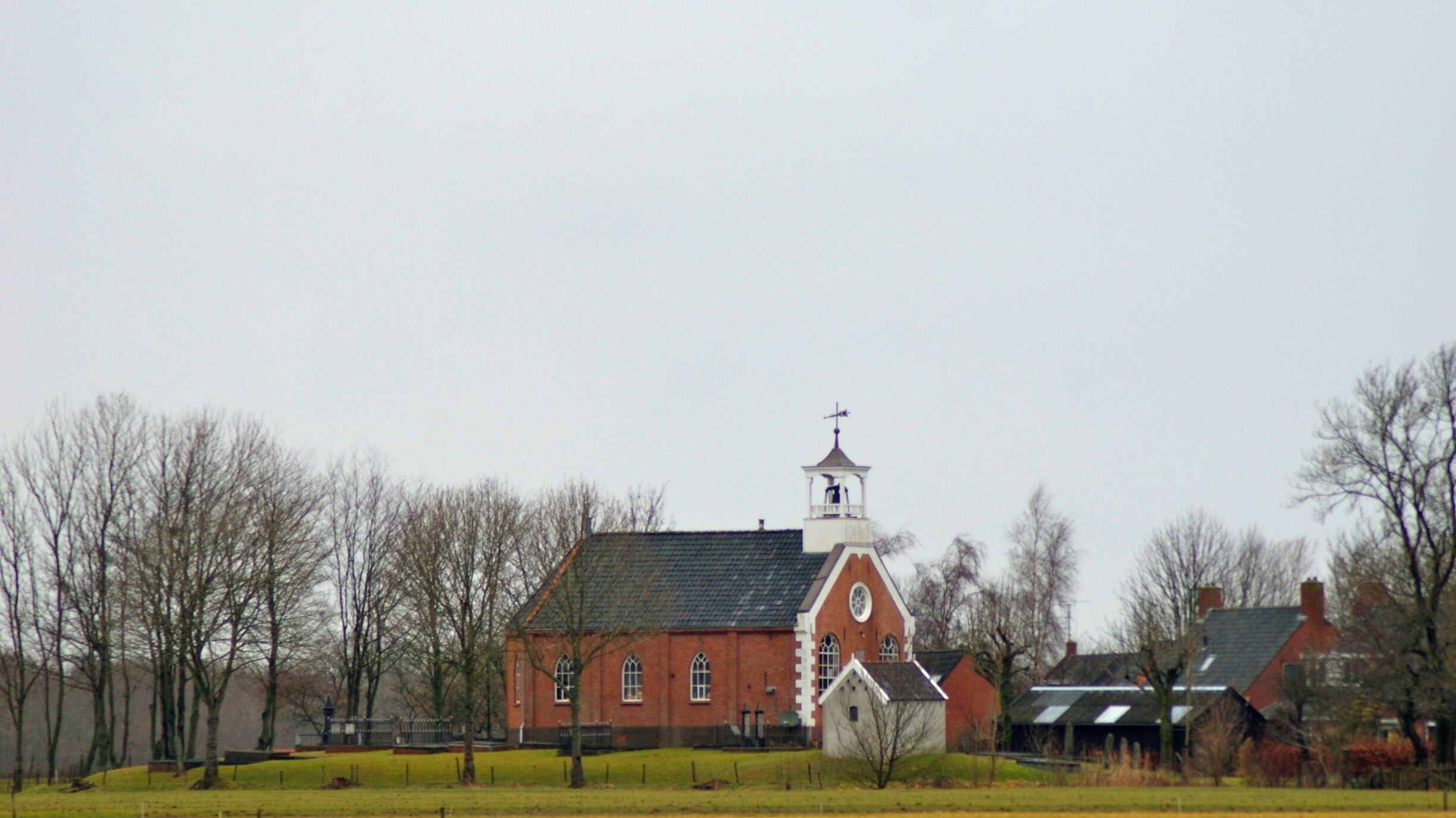 A red brick church with a white steeple and a small bell tower.