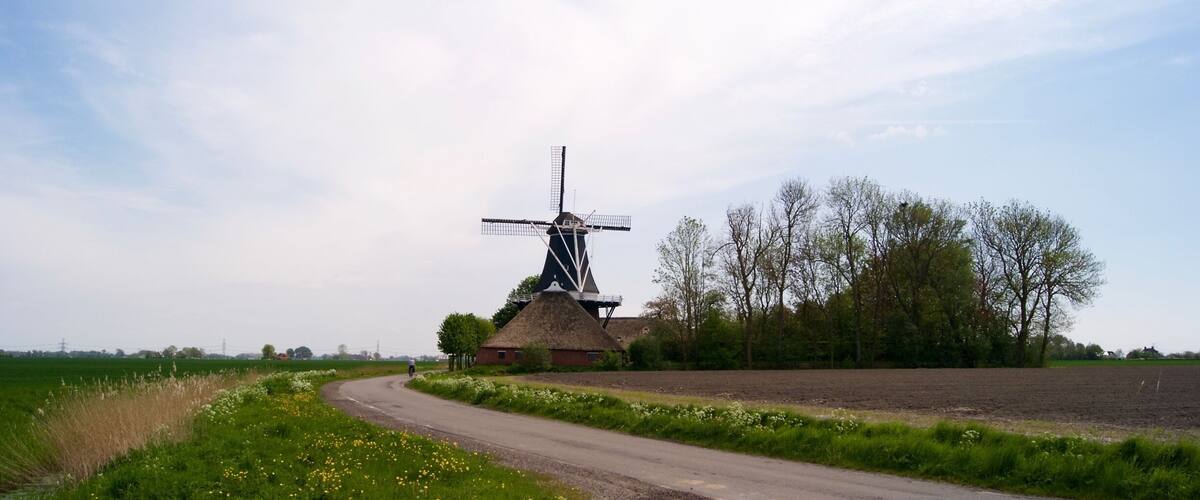 A rural landscape with a windmill, a thatched-roof building, and a winding road.