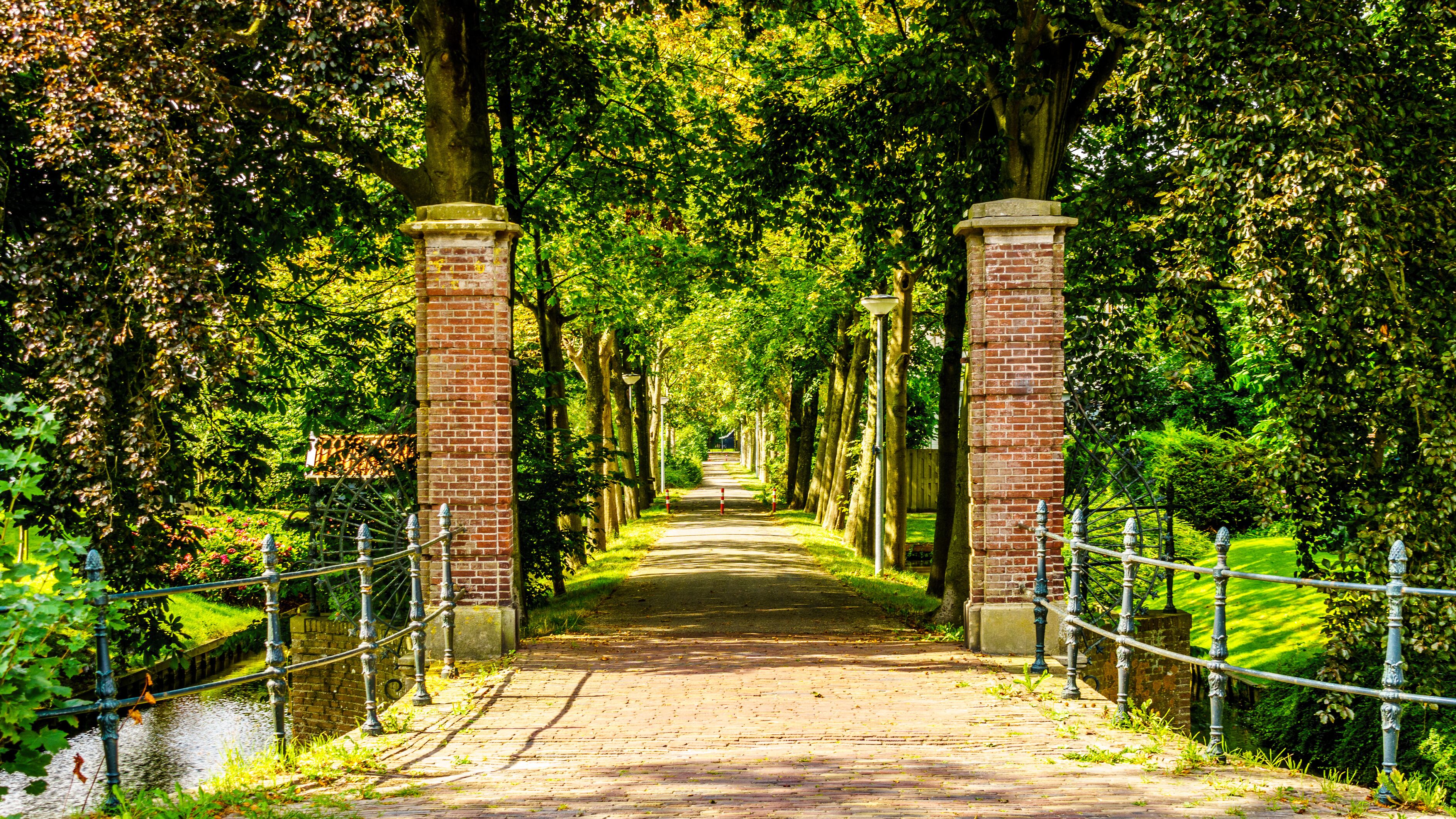 A tree-lined pathway with brick pillars and a rope barrier.
