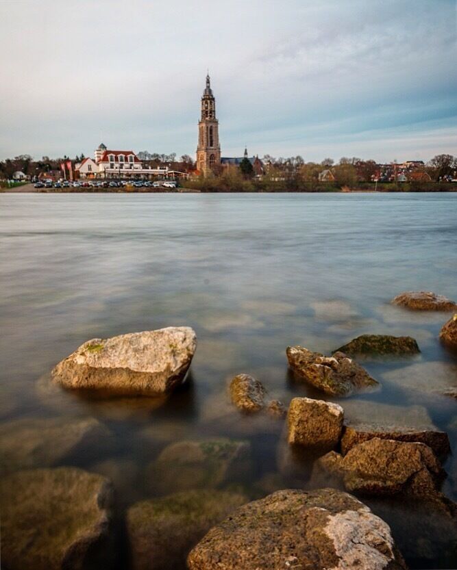 A calm river with rocks in the foreground and a tower in the background.