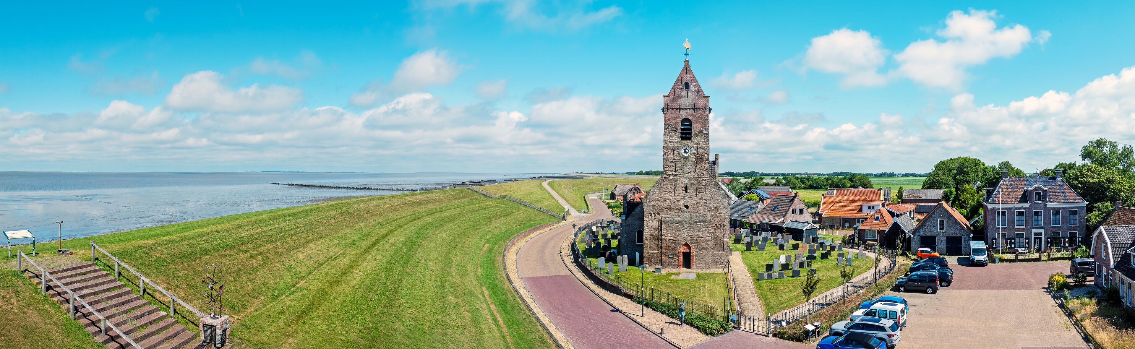 A coastal town with a prominent church tower, a cemetery, and houses along the waterfront.