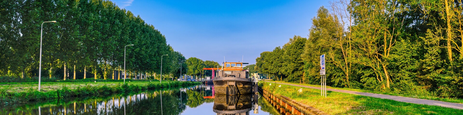 Un canal estrecho con un bote, rodeado de árboles y un cielo azul despejado.