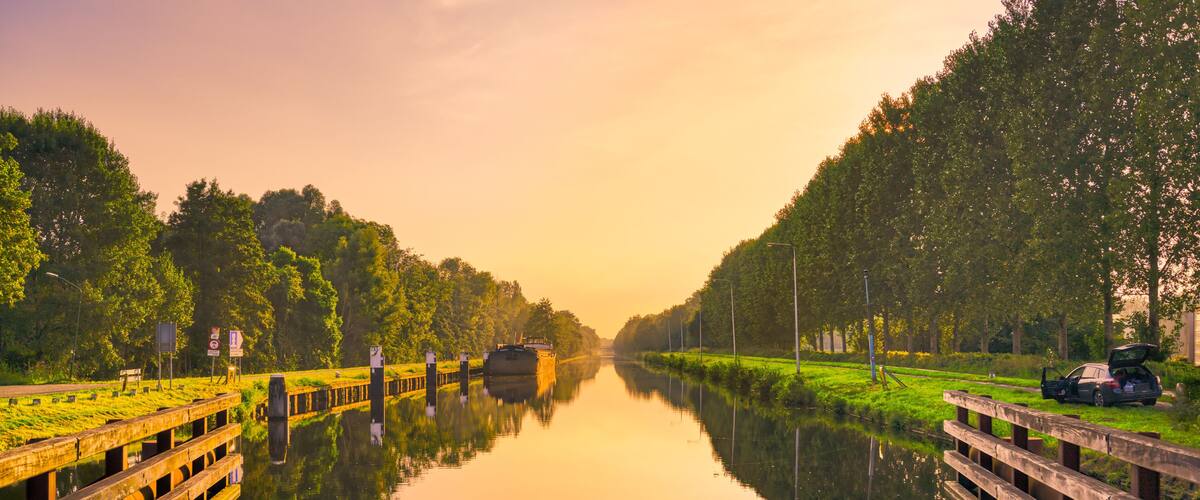 A calm river with a boat, surrounded by lush greenery and a wooden bridge.