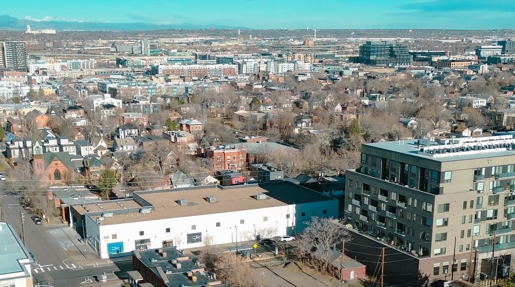 Panorama aerial view neighborhood blocks near Curtis Park extend toward high rise clusters along Champa St. Clear skies brighten varied roofs HVAC units, brick tones, seasonal foliage, Denver, CO
