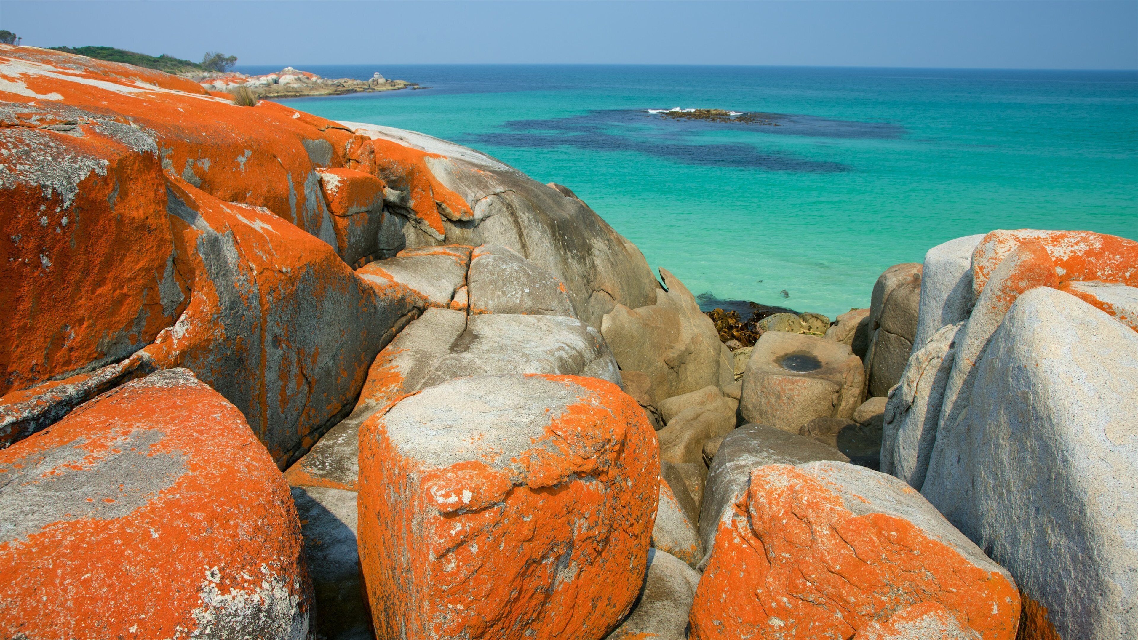 A rocky coastline with orange lichen-covered boulders and turquoise waters.