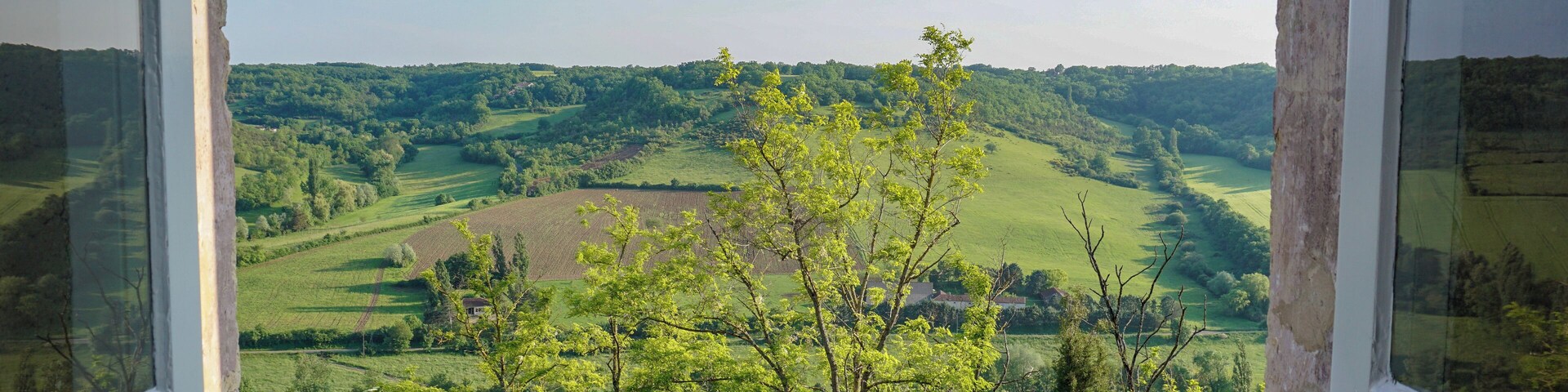 Vista desde un balcón sobre un valle verde con árboles y campos.