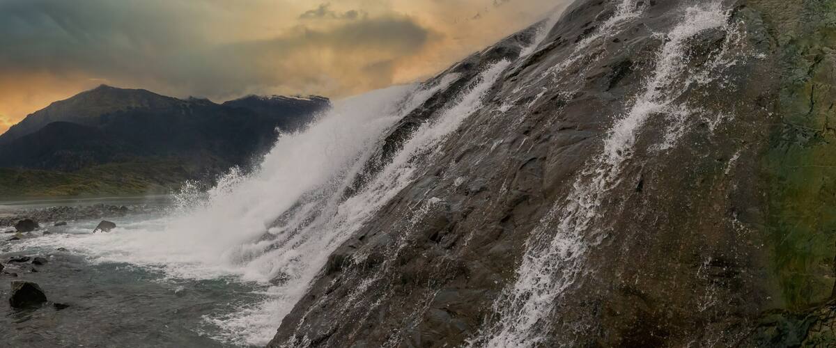 A waterfall cascading down a rocky slope with a sunset in the background.