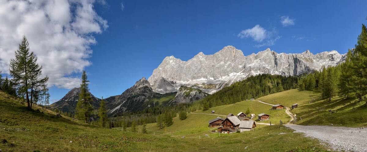 A mountain landscape with a clear sky, a gravel path, and wooden houses on a hillside.