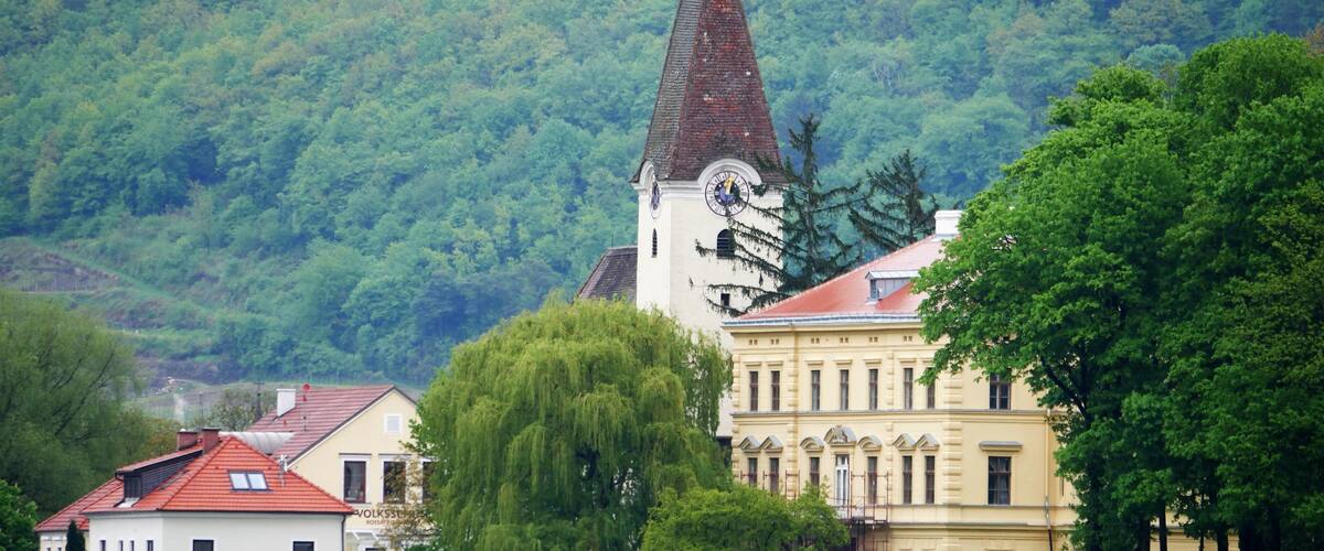 A church with a clock tower, surrounded by lush greenery and traditional buildings.