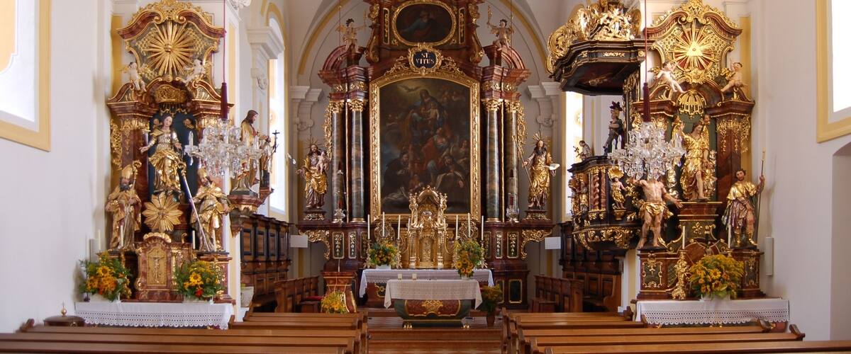 An ornate church interior with a high altar, religious statues, and a large mural.