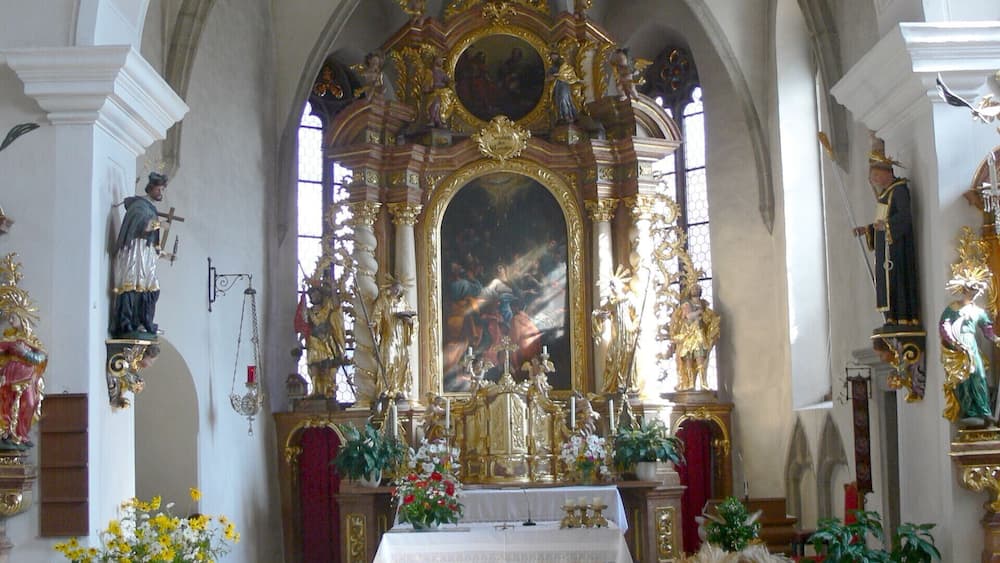 An ornate church interior with a high altar, religious statues, and floral decorations.