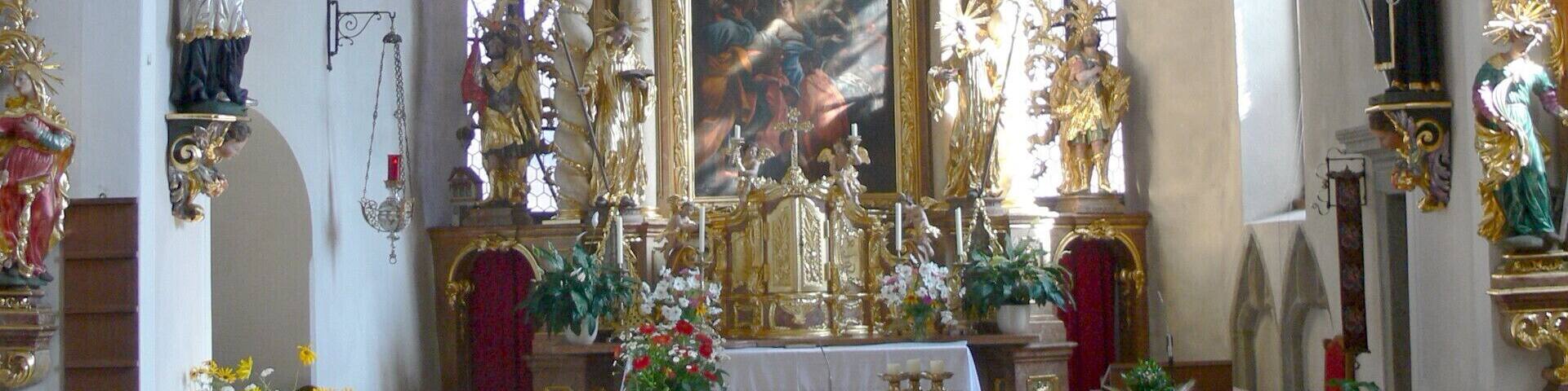 An ornate church interior with a high altar, religious statues, and floral decorations.