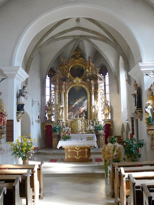 An ornate church interior with a high altar, religious statues, and floral decorations.
