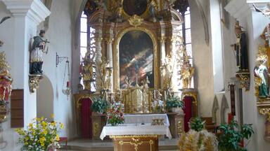 Interior ornamentado de una iglesia con un altar mayor, estatuas religiosas y adornos florales.