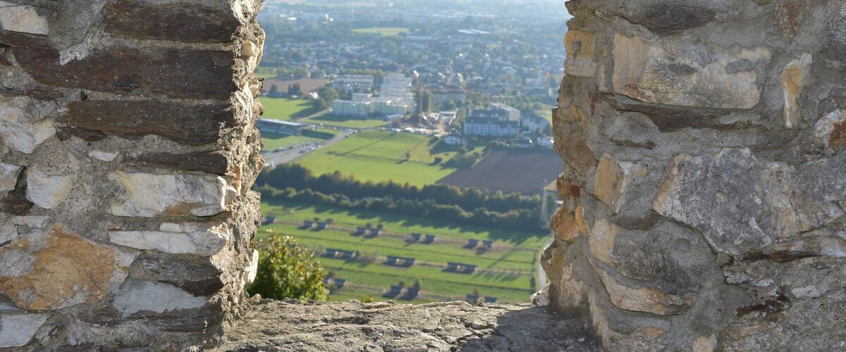 A stone archway overlooking a valley with fields and distant buildings.