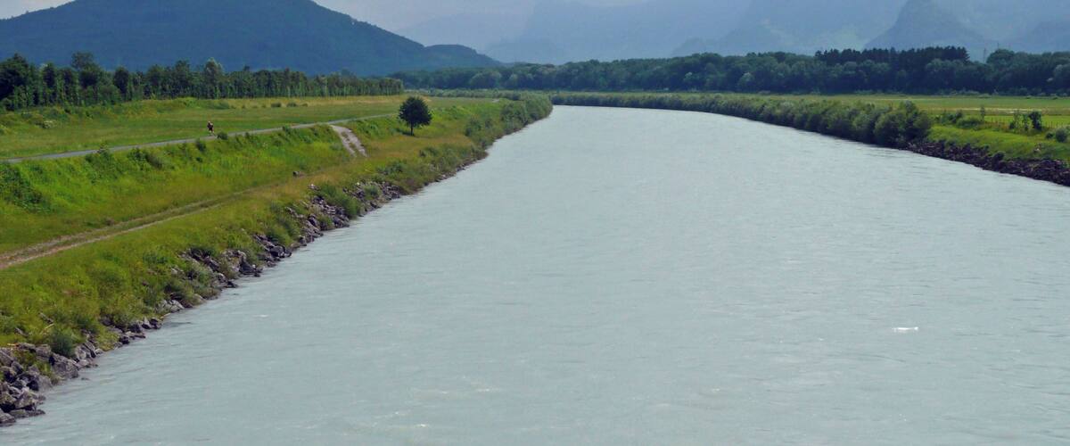 A river flowing through a green landscape with mountains in the background.