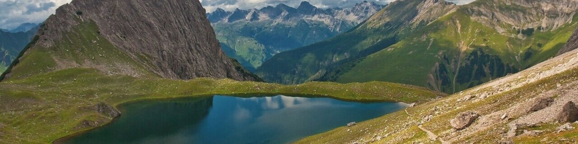 July 2015
Kogelsee, Lechtaler Alps
Kogelsee lake in 2.171 m altitude is one of the many lakes in Lechtaler Alps in Tirol, Austria. On the left the Kogel (2.318 m) and to the right the green meadows of Taja Spítze (2.352 m). In the background in middle there are the Allgaeuer Alps behind the Lech river valley (= Lechtal).
This is the route from Gramais village (1.437 m) to Hanauer Huette over Kogelseescharte saddle. It is a demanding 5 hours trek, day 1 of our 4-days trek in Lechtaler Alps this summer.
