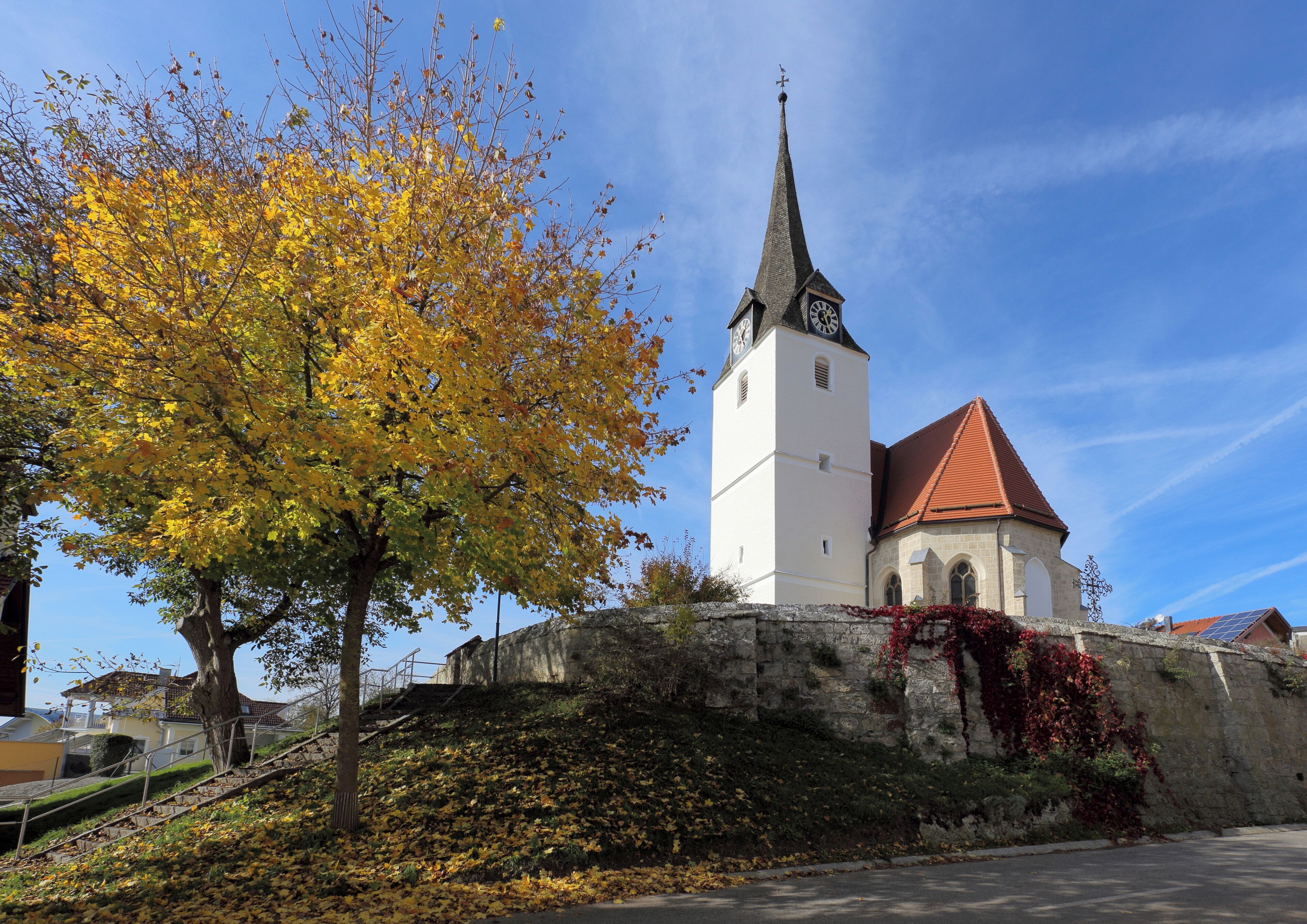 A church with a clock tower, surrounded by autumn foliage and a stone wall.