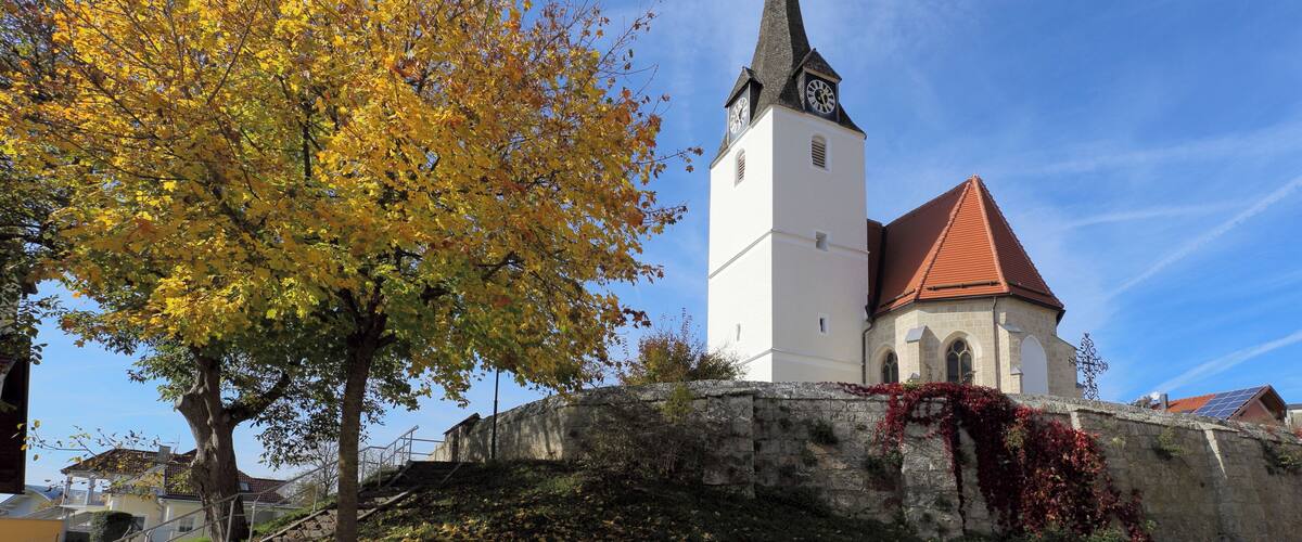 A church with a clock tower, surrounded by autumn foliage and a stone wall.