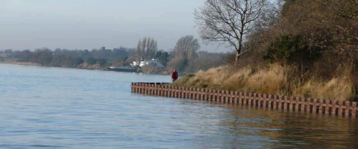 A calm river with a wooden walkway and a person walking.