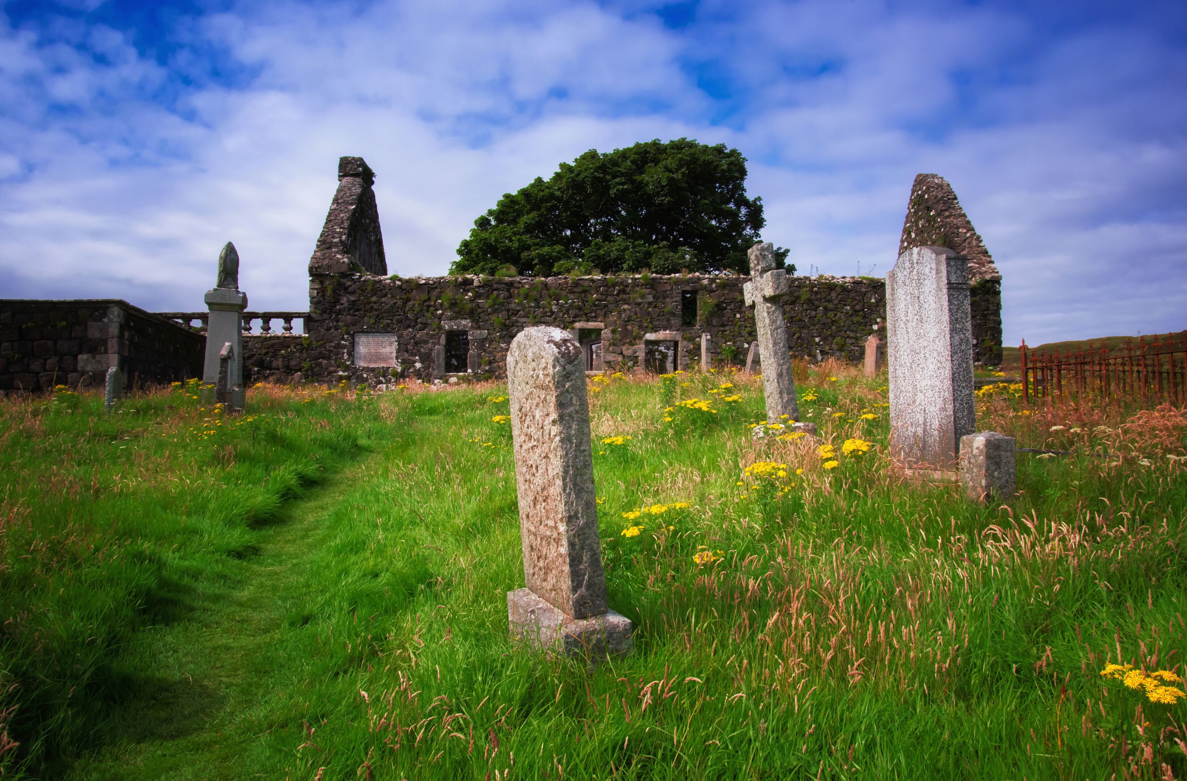 A historic stone structure with ruins and standing stones in a grassy field.