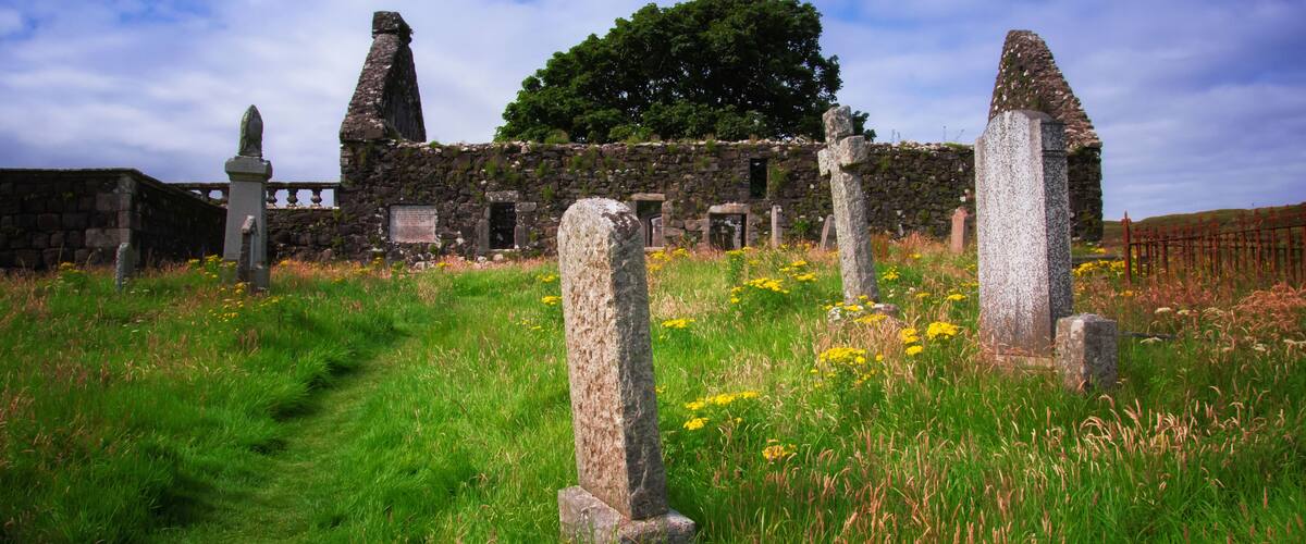 A historic stone structure with ruins and standing stones in a grassy field.