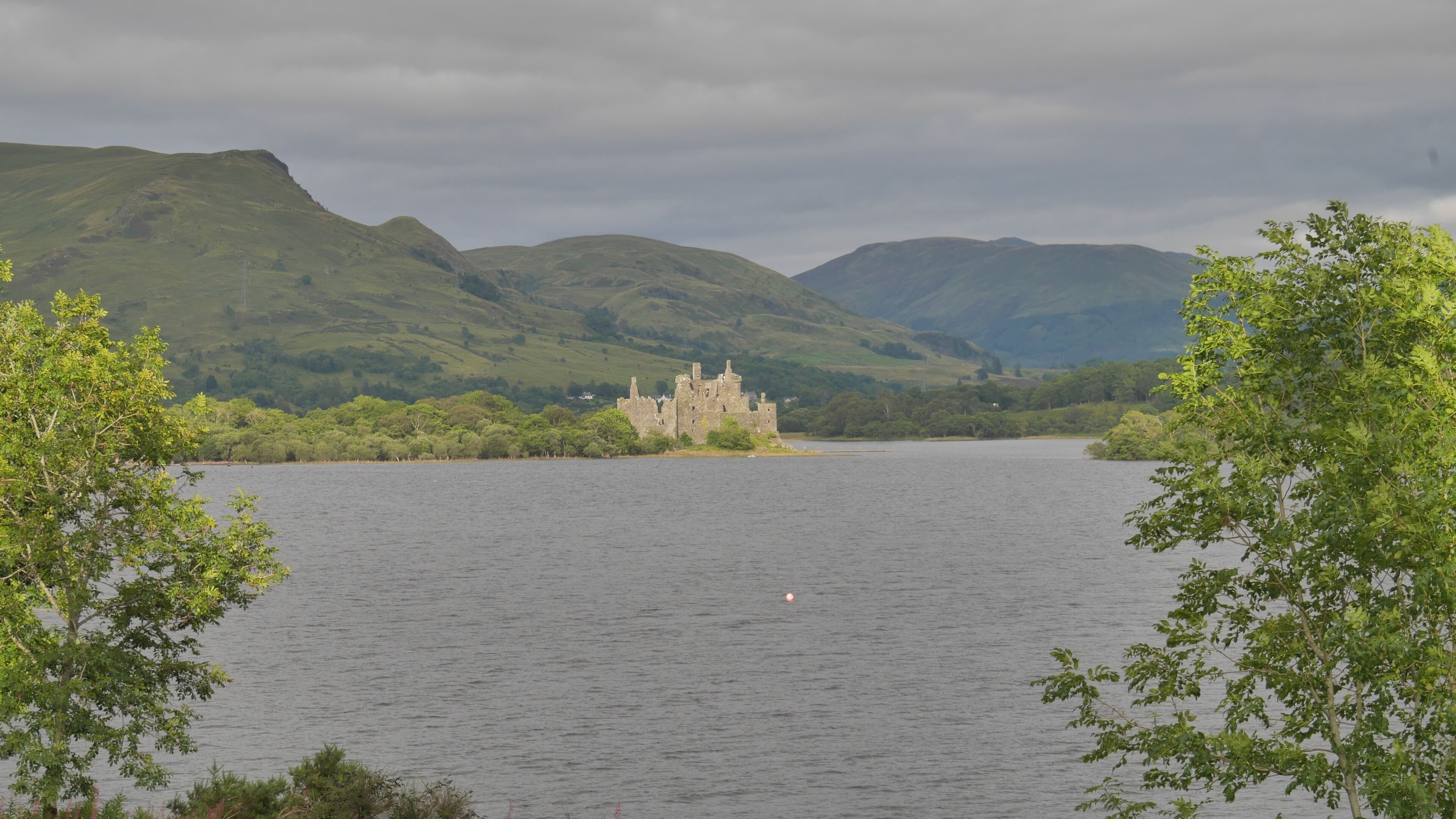 A castle on a lake surrounded by hills.