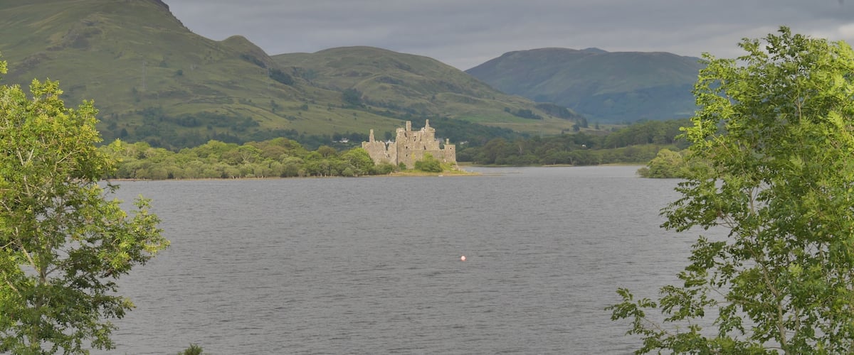 A castle on a lake surrounded by hills.