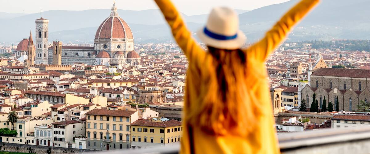 A person with arms raised, overlooking a cityscape with prominent domed buildings and a river.