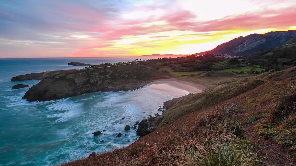 Un paysage côtier avec une plage, une côte rocheuse et un coucher de soleil.